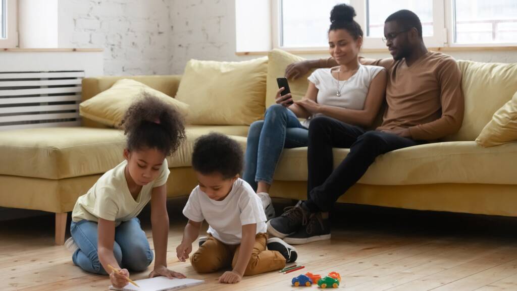 Kids drawing sitting on warm floor parents resting on couch